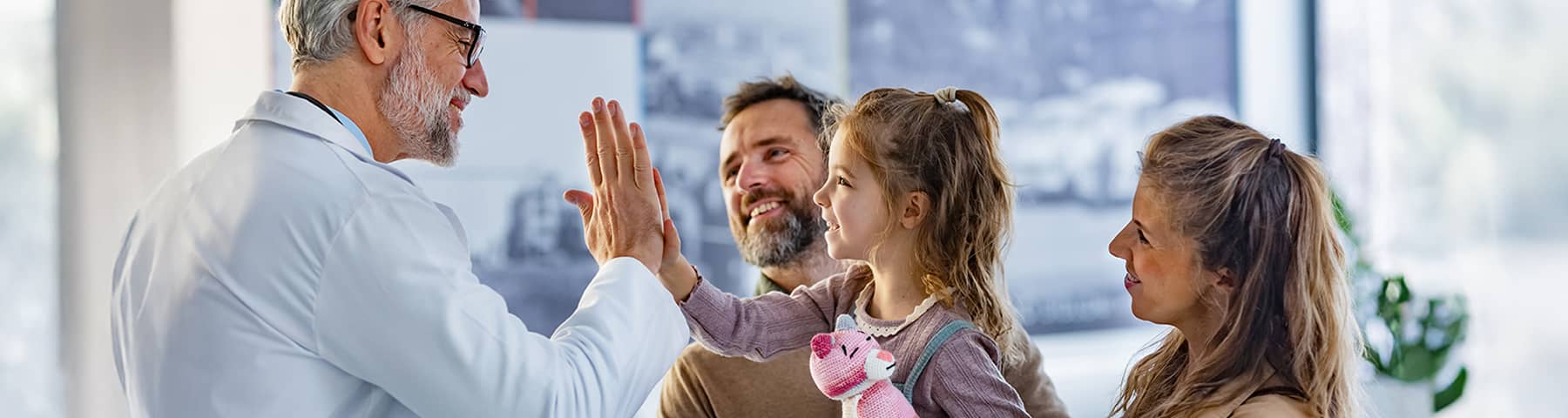 Doctor high-fiving a young girl while her parents smile in a clinic.