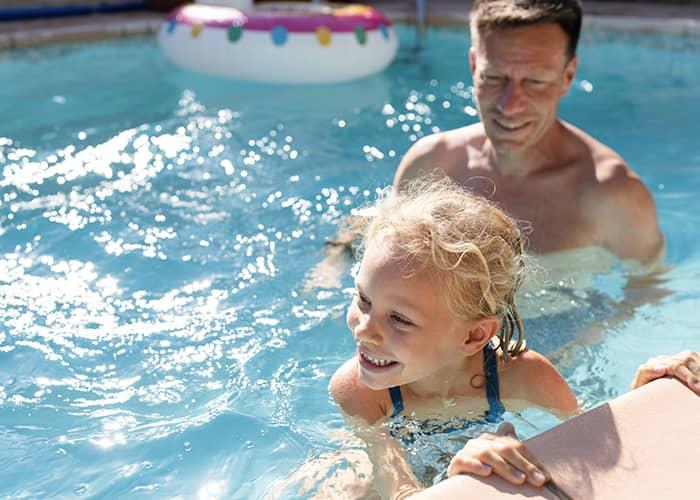 A smiling child and an adult enjoying time together in a swimming pool, highlighting supervision and water safety.