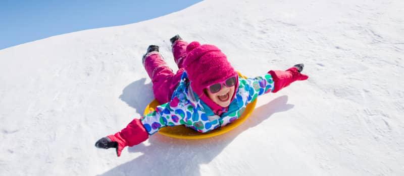 Little girl riding on snow slides in winter time