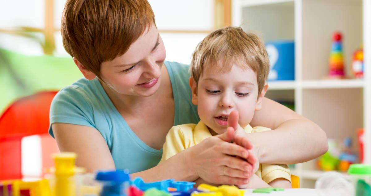 Woman helping a child play with modeling clay.