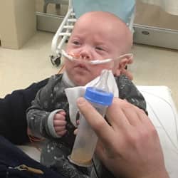 Hunter with with tubes in nostrils while dad is bottle feeding him.